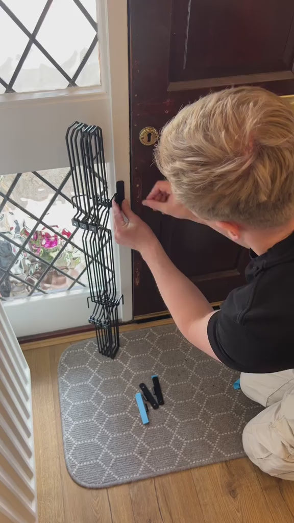 Installing Dog Safety Gate Plus at a front door with adhesive brackets, dog waiting behind the gate